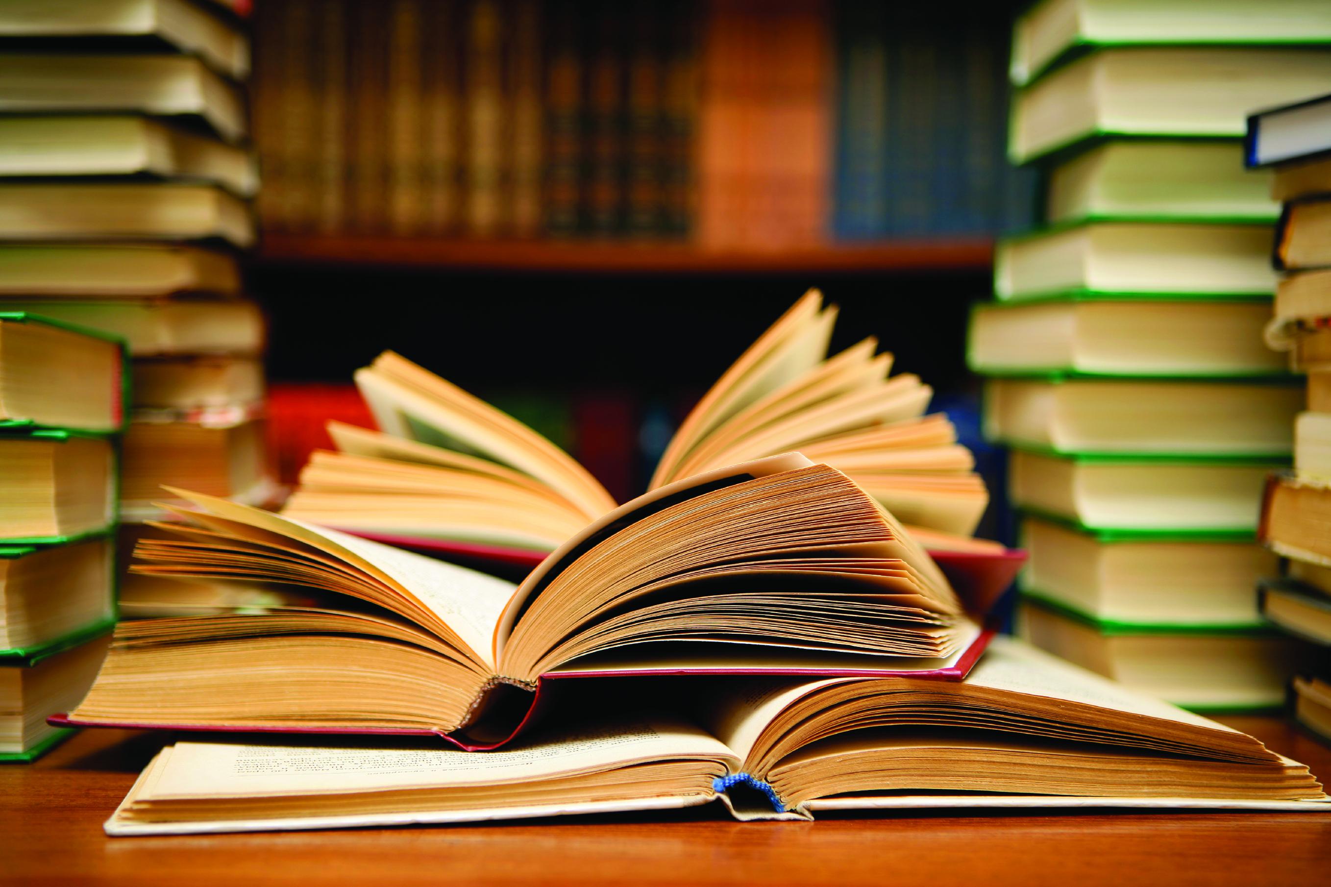 Stacks of books and several open books on a table.