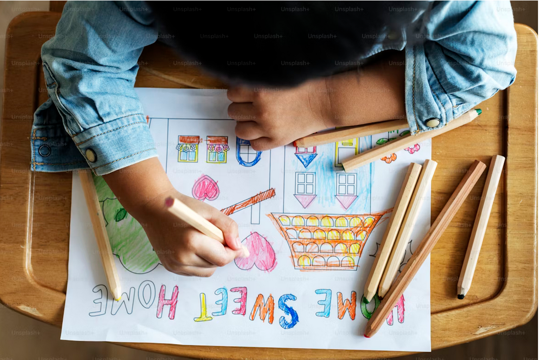 An overhead view of a child coloring a drawing that says home sweet home.